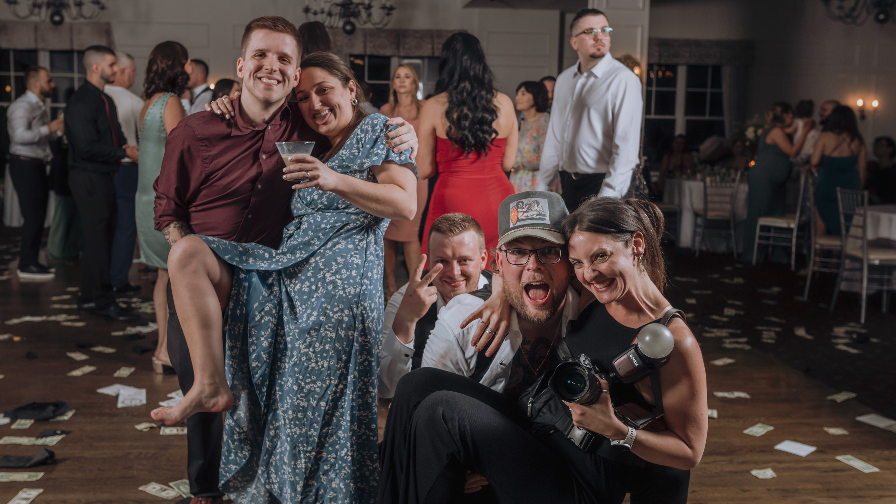 Cam and Maggie of Two Friends Photography laughing with a couple and guests on a wedding dance floor scattered with money