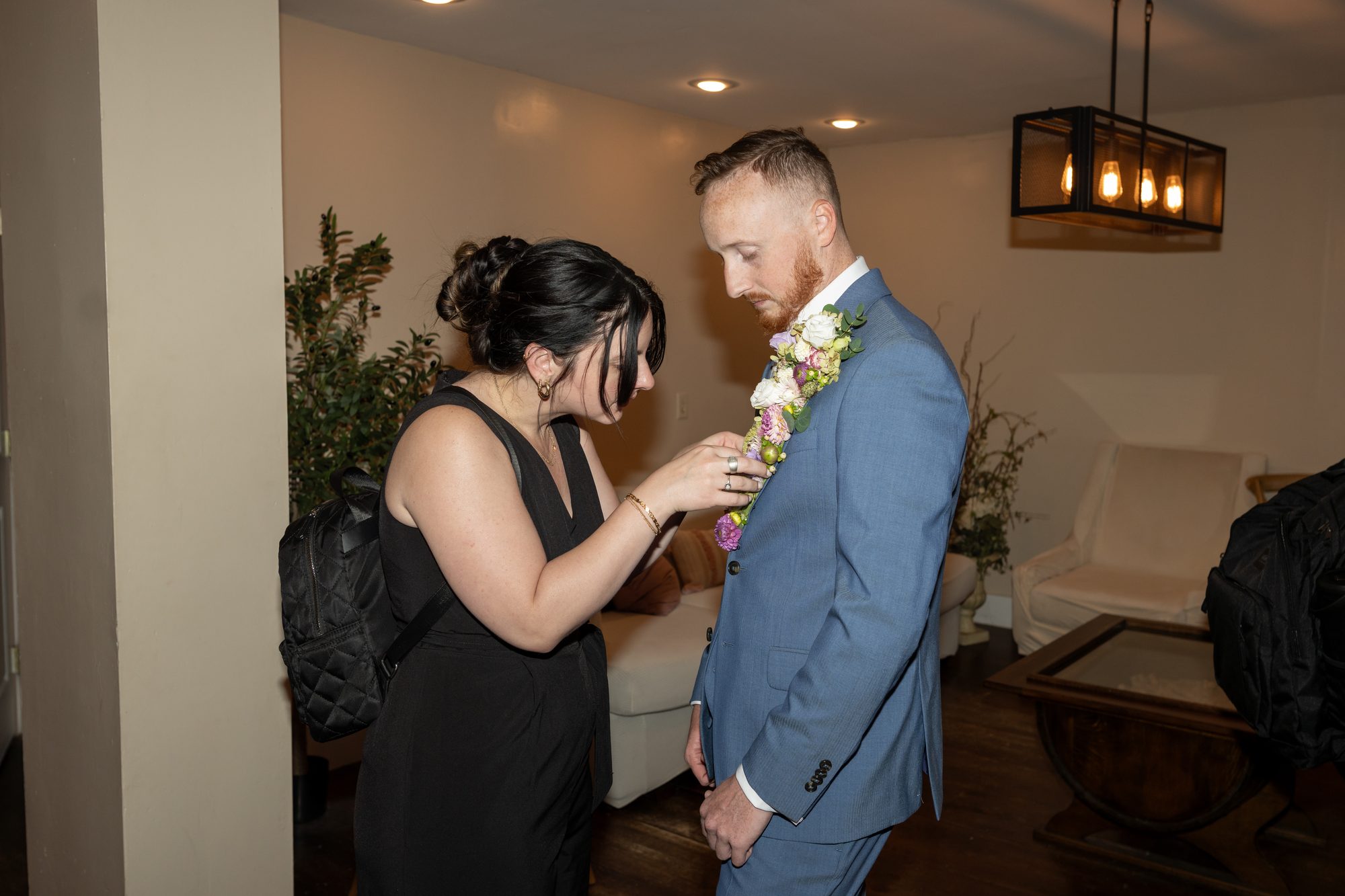 Maggie of Two Friends Photography pinning a floral boutonnière onto a groom in a blue suit before a wedding